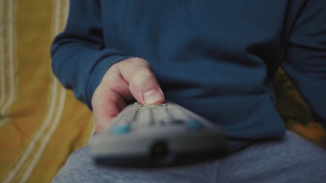 Close up of a hand clicking buttons on a TV remote control to change channels.