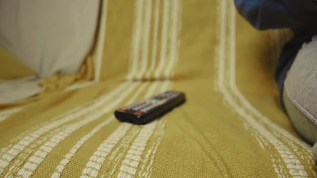 Close up of a hand clicking buttons on a TV remote control to change channels.