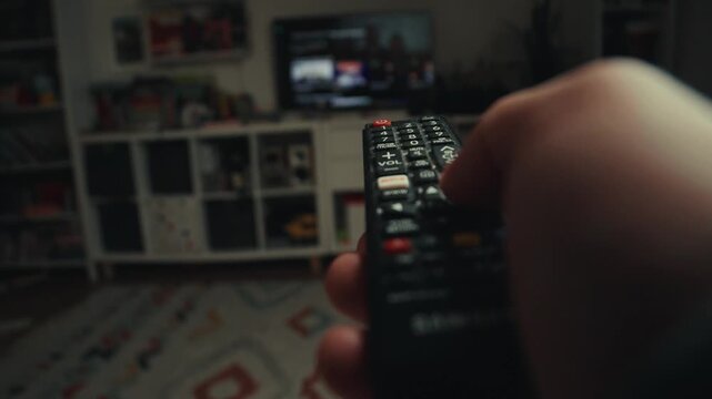 Close up of a hand clicking buttons on a TV remote control to change channels.