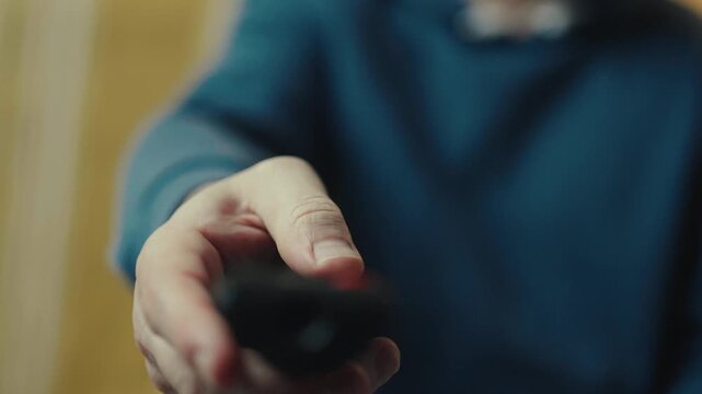 Close up of a hand clicking buttons on a TV remote control to change channels.