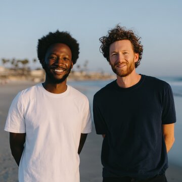 Two adult male african and caucasian friends at sunset on the beach together adult males smiling coastal portrait in warm light by the sea