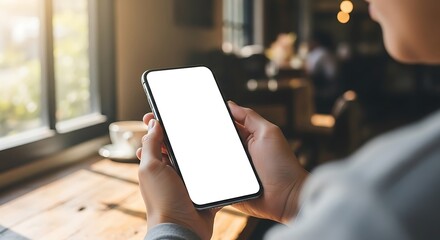Person holding a smartphone with a blank white screen mockup in a cafe