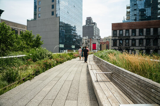 People walking along the High Line elevated park surrounded by greenery and modern buildings in New York City. Urban park pathway offers scenic views of Manhattan architecture and city life.