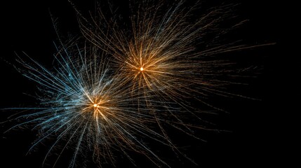 Obraz premium Twin bursts of golden and blue pyrotechnic sparks illuminate a dark night sky.