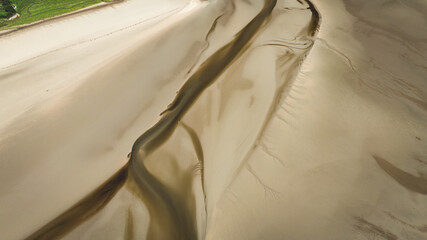 Aerial view of tidal flats with winding water channels and green coastal landscape