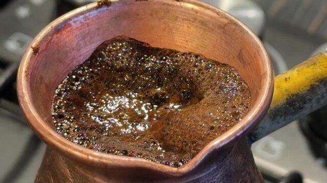 freshly ground coffee beans are boiling in an old copper coffee pot with foam