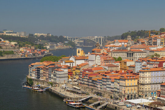 Vista elevada del casco hist&oacute;rico de Oporto, mostrando las casas coloridas de la Ribeira, los barcos en el r&iacute;o Duero y el puente de la Arr&aacute;bida al fondo bajo un cielo despejado.