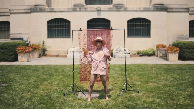 Confident androgynous man in a pink outfit dancing vogue in a formal garden on a sunny day