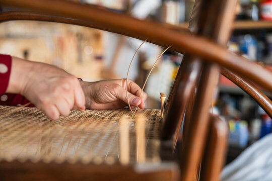 Artisan's hands meticulously weaving rattan fiber, restoring a vintage thonet style chair seat, showcasing traditional craftsmanship