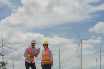 Two Engineer wearing safety helmets and using laptop while inspecting wind turbines, windmill at renewable energy farm, concept of teamwork, green technology, sustainable power. engineer, wind turbine