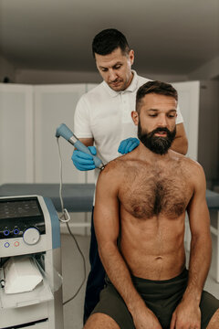 Physiotherapist treating man's shoulder with shockwave therapy equipment