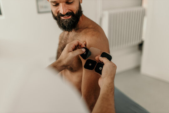 Physiotherapist applying electrostimulation pads on man's shoulder