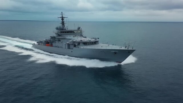 Aerial drone view of naval warship speeding across open sea.
