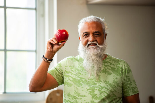 Indian stylish man pointing at apple and demonstrating fitness in kitchen