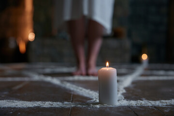 Candlelit chalk circle with barefoot practitioner standing near stone hearth