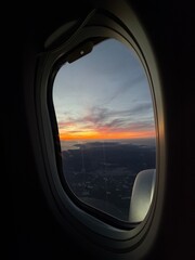 Fototapeta premium View from an airplane window during sunset, warm golden light reflecting on the aircraft wing, dramatic clouds and colorful sky, high-resolution travel photography.