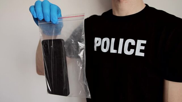 Police officer in gloves with a smartphone into an evidence bag. Concept of data security and cybercrime