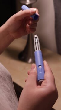 A vertical close up of a young woman screws a needle on pre-filled pen injector with semaglutide to prepare it for taking medicine