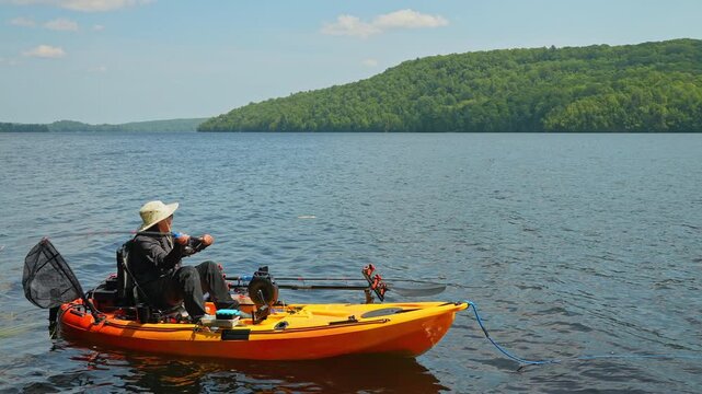 Woman enjoys kayak fishing at scenic coastline, casting her rod and reeling. Peaceful water shore and perfect setting at lake, Ontario, Canada. Catch and release fish. Kayak sport fishing.