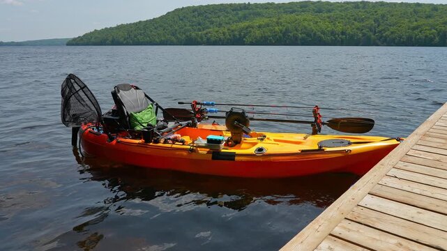 Fully rigged kayak watercraft mooring and tied to boat pier near cottage. Recreational watercraft, kayaking lake during tournament or fishing derby. Kayak water craft equipment for fishing activities.