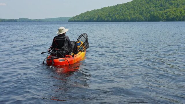 Woman floating on kayak boat. Kayaking lake with scenic landscape.  Woman angler in a sun hat on motorized kayak enjoying peaceful summer vacation sunny day while active outdoor.