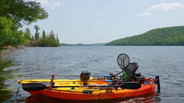 Fully rigged kayak watercraft mooring and tied to boat pier near cottage. Recreational watercraft, kayaking lake during tournament or fishing derby. Kayak water craft equipment for fishing activities.