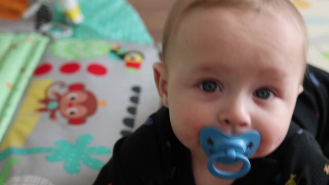Tranquil Infant Gazes Softly On Nursery Mat. Baby Peacefully Lying With Blue Pacifier In Gentle Nursery Setting