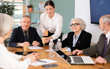 Obraz premium Elderly woman sits at conference table leading business meeting with group of elderly men and women