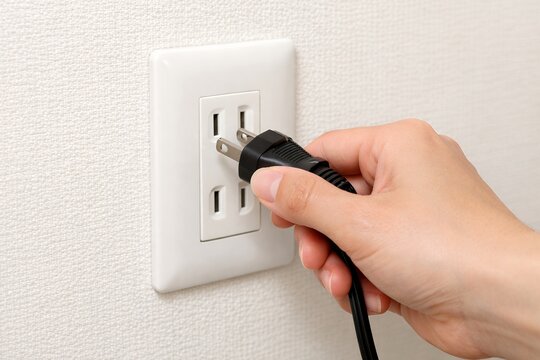 壁のコンセントに電源プラグを差し込もうとする日本人の手元と家電の黒いコードのクローズアップ