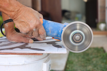 Close up of worker cutting ceramic tile with an angle grinder during home renovation. Tile installation process, construction work, DIY flooring and professional building tools.