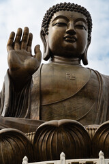 Fototapeta premium A close-up of the Tian Tan Buddha (Big Buddha) bronze statue at Ngong Ping, showing the raised right hand, serene face and intricately carved robe with a swastika symbol on the chest, Hong Kong