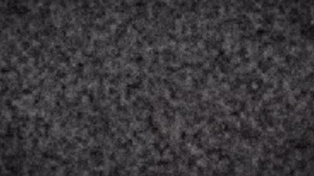 4K Alpha Channel Glitch close-up of dark grainy texture surface showing dense irregular shapes on rough asphalt-like material in dim studio setting