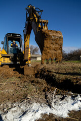 Fototapeta premium Excavator Bucket Covered in Soil Digging Trench on Sunny Construction Site