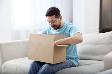 Happy man opening parcel on sofa at home