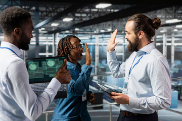Diverse pleased staff sharing a high five to enjoy their accomplishment on server farm industrial...