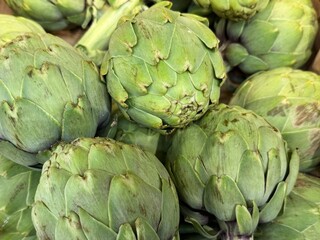 Obraz premium Fresh green artichokes close up at farmers market. Organic seasonal vegetables used in Mediterranean cuisine. Concept of healthy food, fresh produce, plant based diet and natural ingredients.