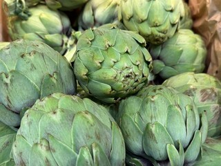 Obraz premium Fresh green artichokes close up at farmers market. Organic seasonal vegetables used in Mediterranean cuisine. Concept of healthy food, fresh produce, plant based diet and natural ingredients.