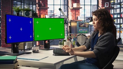 Professional woman works at modern workspace using green screen on dual monitors setup. High tech...