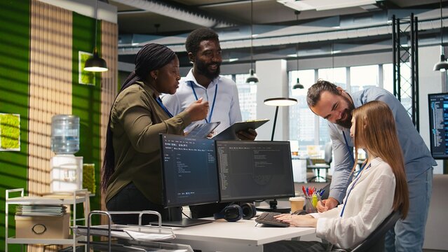 Friendly coworkers helping junior dev code AI algorithms to debug software issues and improve systems, teamwork concept. Welcoming team assisting newcomer in tech startup office, camera A