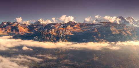 Panoramic aerial view of the Swiss Alps with snow-capped peaks and low clouds at sunset. Bright...
