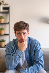 Fototapeta premium Upset man feeling lonely or thinking about problems. Bad feelings stress, anxiety, grief, emotions. Handsome millennial guy, feeling wrong and alone at home sitting on couch