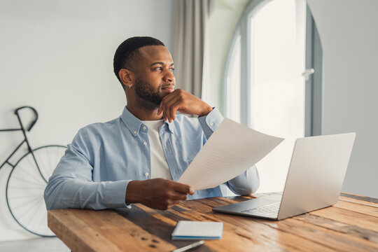 Happy smiling cheerful African American man reading letter at workplace, sitting at work desk, satisfied businessman received good news, job promotion, money refund or great exam results