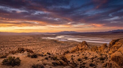 View of river winding through desert landscape at sunset with mountains in the distance