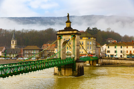 View of old suspension bridge with statue of Virgin Mary across Rhone river and embankment of Seyssel on winter day, Ain department, France