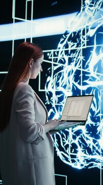 Vertical video Engineer reports to AI brain automated manager displayed on digital dashboard. Woman completes assignments distributed by artificial intelligence agent superintelligence using laptop