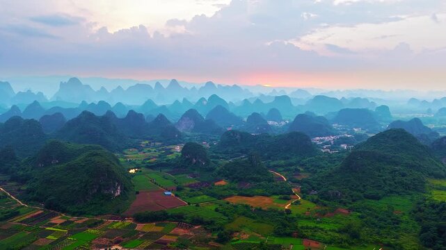 Panoramic aerial view of lush karst mountain peaks and agricultural fields in Guilin, China at sunset.