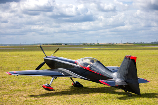 Gamebird GB1 aerobatic plane parked on a grassy airfield with pilot and wind turbines.
