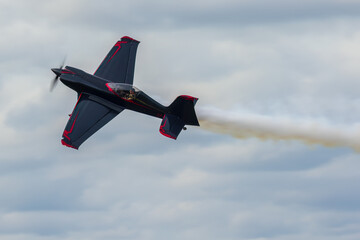 Gamebird GB1 aerobatic plane performs against a cloudy sky, leaving a smoke trail.