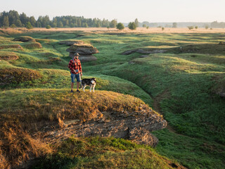 Drone view of a man and his husky dog standing on a limestone cliff in the scenic green Estonian landscape. © Dmitri