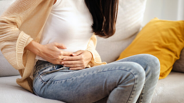 The image depicts an interesting young woman experiencing abdominal pain, menstrual cramps, or other types of abdominal pain.